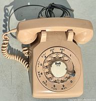 Top-down view showing the rotary dial with Bell (416) logo, beige body, and coiled handset cord.