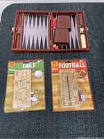 Photo showing backgammon set open with dice, checkers, dice cups and golfing and football travel games in packaging.