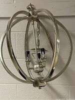 Full view of spherical chandelier light fixture showing the metal circular bands and mounting chain with electrical wiring.