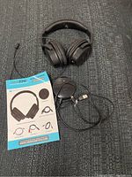 Over-ear black wireless headphones with instructions and cables on gray textured surface