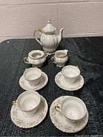 Full view of the tea set arranged on black textured cloth, showing the teapot with lid, sugar bowl, creamer, and four tea cups with saucers.