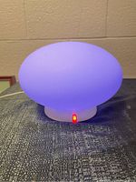 Oval light emitting blue hue on a textured surface with red LED power indicator lit at base.