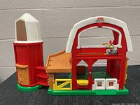 Full view of the Fisher Price barn and red silo made of plastic with textured details and colors red, white, green, and yellow.