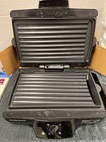 Open Hamilton Beach indoor grill showing ribbed grill plates on top and bottom grilling surfaces.