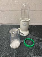 White Isa blender base with tall clear jar and fitted lid assembled on top, sitting on a dark surface with textured wall background.