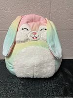 Front view of medium-sized colorful bunny Squishmallow plush with closed eyes and smiling face.