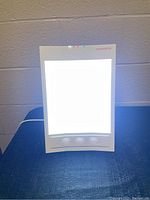 Bright light therapy lamp front glowing brightly, rectangular with white frame.