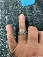 Ring worn on a finger showing size and fit with large central stone and halo design.