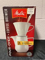 Front view of the box showing Melitta logo, image of white porcelain brewing cone and carafe, and 6-cup capacity label.