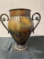 Front view of the rustic metal vase showing the bulbous ribbed body, curled handles, and pedestal base.