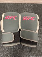 Front side view of UFC fight gloves showing grey palm padding and pink UFC logo on back with wrist straps.