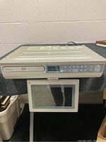 Front view of beige Venturer DVD player showing flip-down LCD screen and control buttons