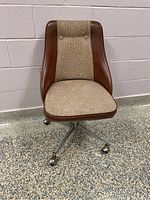 Side angle of the vintage swivel chair showing the upholstery and metal base with casters.