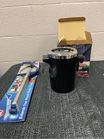 Photo of black wine chiller with silver rim and open box behind, along with metal wine bottle grabber on the side.