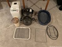 Full lot viewed from above showing white bread maker, black slow cooker, food processor, blue speckled roasting pot, black cooking pot with lid, white blender/chopper, and three wire racks.