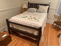 Full view of the double size bed made with floral bedding, pillows and dark wooden frame in a room with hardwood floor.