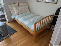 Full view of twin size wooden bed frame with bedding including duvet and pillows