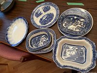 Image showing six vintage blue willow serving dishes arranged on table, including one non-blue willow oval platter.