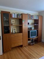 Front view of entire multi-section wooden cabinet with shelves, three tall cabinets, and dresser drawers filled with books and decor.