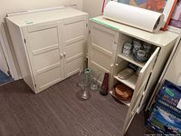 Three white IKEA cabinets positioned near a wall with assorted glassware and ceramic dishes nearby, one cabinet with glass doors visibly broken on the bottom right panel.