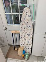 Ironing board, Phillips iron, wooden drying rack, and netted drying rack near a door and white cabinetry.