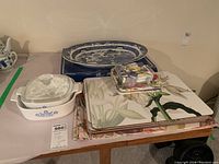 Overview photo showing two Corningware casserole dishes, Blue Willow platter, placemats, disposable plates and napkins arranged on a table.