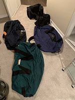 Overview of all five duffel bags on beige carpet floor, showing size and color variations
