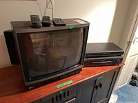 Toshiba 20-inch CRT TV, Toshiba DVD player, Panasonic VHS player on a wooden surface, all with remotes on top of TV.