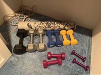 Photo of all dumbbells sets and yoga mat on carpet showing weight details and colors.