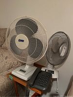 Two fans and one Sony desktop phone photographed on a small table beside a couch, showing the full items for sale.