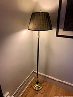 Tall metal floor lamp with black fabric shade and brass base.