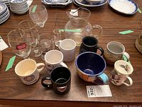 Assorted mugs, glasses, and a large glass pitcher on wooden table