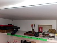 Top shelf showing brown leather folio, black wrist rest, wired and wireless mice, small wooden tray, staplers, carved figure paperweight, and other assorted small office items