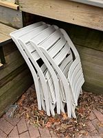 Four white plastic folding patio chairs stacked together, showing some outdoor weathering and surface wear.