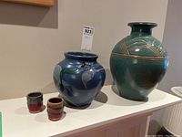 Two vases, green with geometric pattern and blue with floral design, alongside two small cups in red-brown glaze.