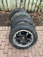 Four tires with rims stacked on brick patio, view of full set
