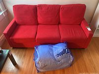 Front view of the red sofa bed with three back cushions and three seat cushions in a bright room with wooden floors.