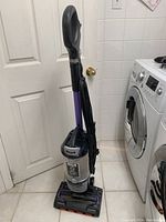 Full view of Shark ZU700C upright vacuum cleaner standing on tile floor, showing handle, dustbin, and base with cord wrapped around the side.