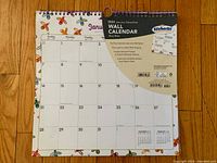 Image of 2024 wall calendar showing January month with colorful floral border, spiral binding, and stickers included on the packaging label.