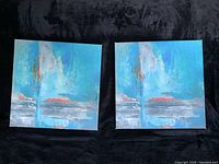 Photo showing two square canvases with abstract blue and white artwork, slight scruffs on edges visible.