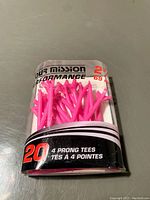 Package of 20 pink 4-prong golf tees in clear plastic container showing branding and quantity.
