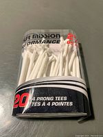 Package of 20 white 4-prong golf tees in clear plastic packaging with branding text showing the number 20 and '4 PRONG TEES'.