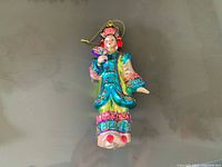 Ornament figurine in full body view showing turquoise dress with pink and gold details and traditional hat with tassels.