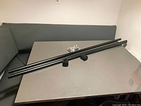 Two black metal curtain rods aligned horizontally on table with mounting hardware placed nearby.