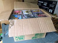 Cardboard box filled with dozens of used jewel case CDs of various artists and genres