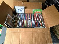 Open cardboard box filled with approximately 50 Christmas music CDs, various artists and compilations in jewel cases.