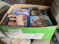 Cardboard box filled with multiple DVDs in cases, various movie titles visible such as 'K-9', 'The Accidental Husband', and others.