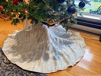 Full view of white Christmas tree skirt under tree on hardwood floor