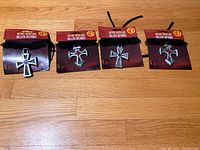 Four new gothic-style necklaces on packaging, showing black cords and plastic cross pendants in two distinct designs: classic pointed crosses and heart-shaped crosses.