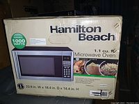 Hamilton Beach microwave oven in box showing front view with model features and specifications.